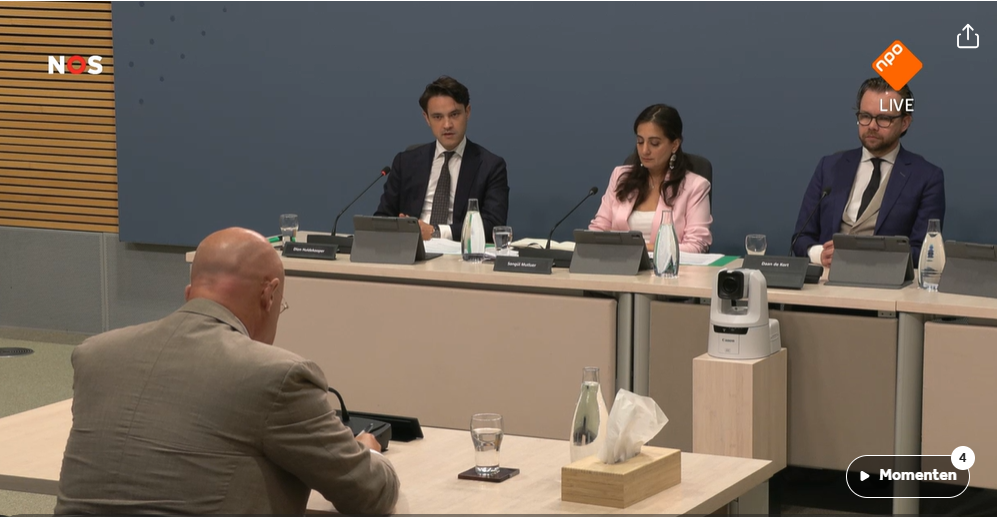 Ferd Grapperhaus tijdens zijn verhoor van de Parlementaire Enquete Corona.
Op de foto is hij van achteren te zien, gezeten tegenover de commissieleden. Naast hem staat nu ook een doos tissues op zijn tafel. Glas water staat er standaard.