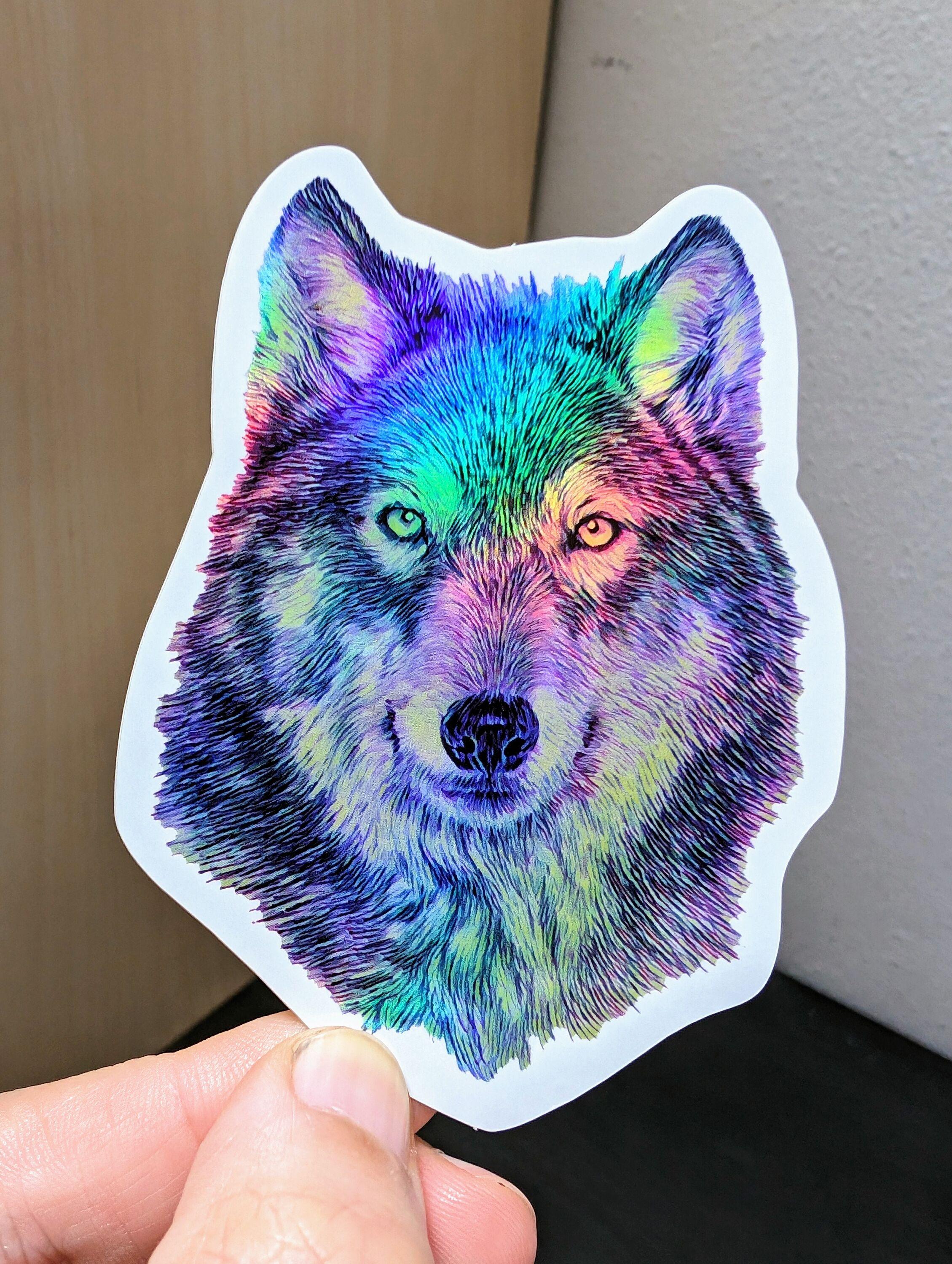Photo of a left hand holding a diecut sticker. The sticker is a holographic wolf drawing.