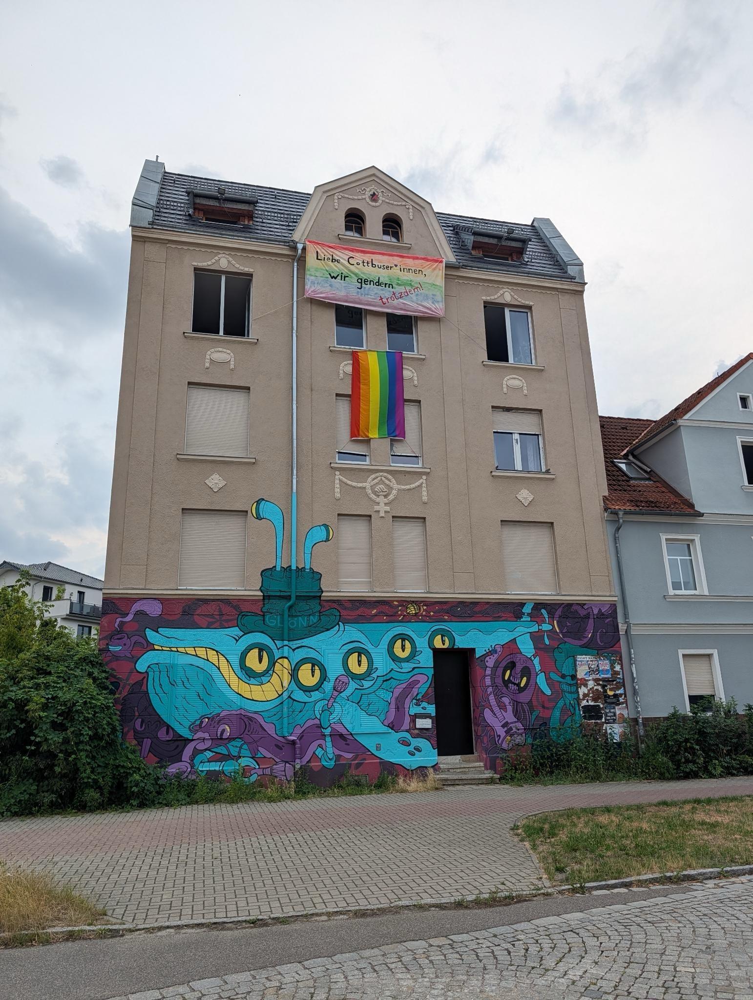 Foto vom Wohnhaus "Zelle 79". Bewohner*innen hatten am Haus ein CSD-Plakat und eine Regenbogen-Flagge aufgehangen. Auf einem Banner nahmen sie Bezug auf die gemeinsame Entscheidung von AfD, Mittelstandsinitiative und Teilen der CDU der Stadtverwaltung das Gendern zu untersagen.