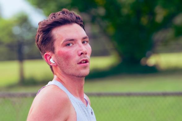 Headshot of man wearing a grey tank top with moderate lengthy hair and iPods looking at me in near-profile