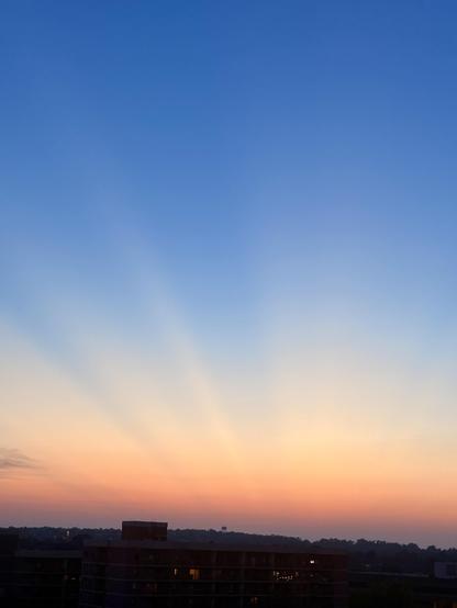 A view of the Courthouse neighborhood of Arlington VA from a high rise. The sun has set in the distance and the sky is blue fading to orange on the horizon. You can see crepuscular rays. 