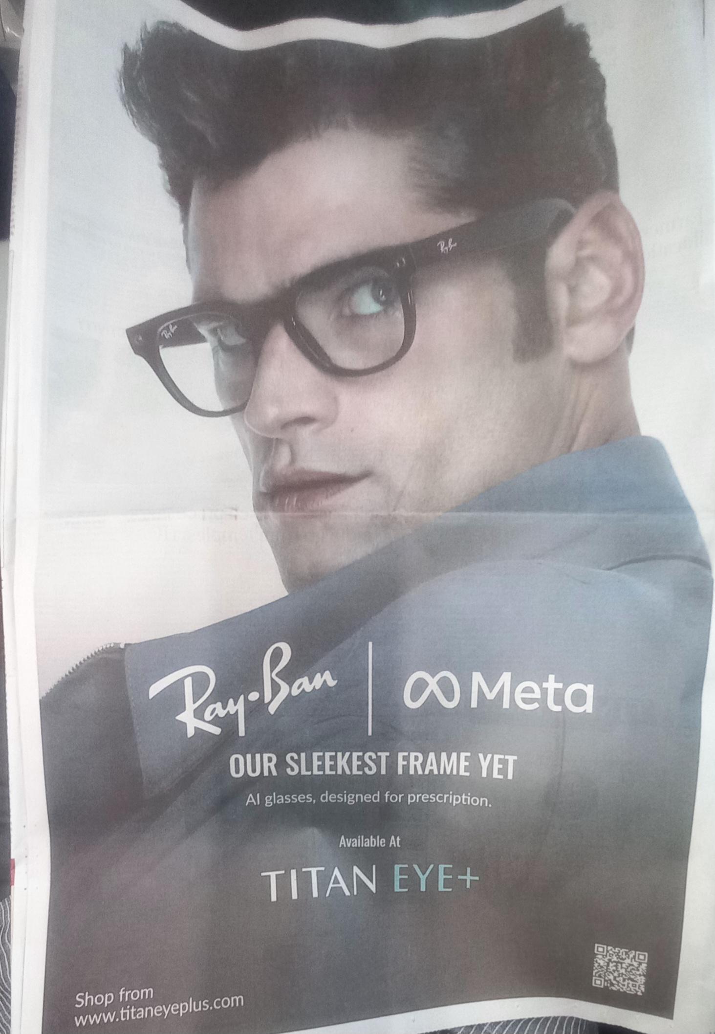 This a full page advertisement for Ray-Ban glases (AI enabled by Meta Glasses)

The ad shows a clean shaving man wearing the same style of Meta Glasses that zukerberge was wearing in the news article of Child abuse ads on Instagram.

The bulk of the image is a faded grey. The top half of the image has the "models" pale face dominating the page,looking over his shoulder at the viewer. 

On the centre is the Ray-Ban Logo (name is the logo) and next to that the Meta creepy glass frame logo withe Meta written next toml it. 

Below thT in all caps "OUR SLEEKEST FRAME YET" 

below that, in sentance case
"AI glasses, designed for prescription" 

Below that two lines 
"Available at" 
"TITAN EYEPLUS" 

***
THE bottom left has "shop from www.titaneyeplus.com" 

The bottom right has QR code (not checked)