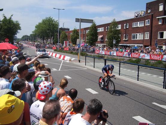 A cyclist wearing a time trial helmet, with a large crowd lining the road