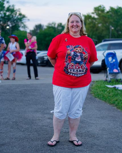 Smiling woman wears a red shirt with a teddy bear that reads "250 years of freedom" with a few more blurred out celebrants behind her.