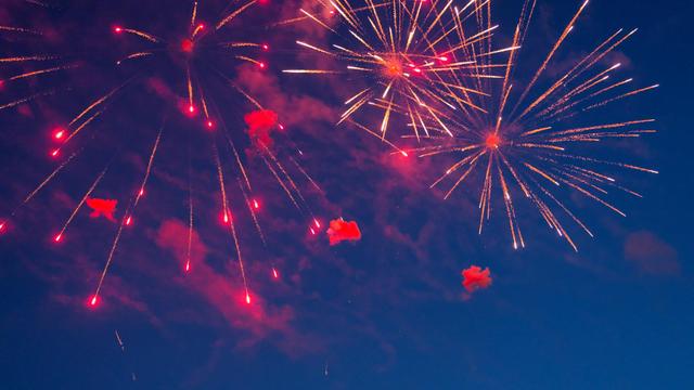 Red and yellow fireworks stream out of three points near the top of the image across a dark blue sky