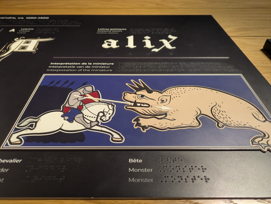 Raised drawing, as well as Braille text in 3 languages (French, Flemish, English), of a knight spearing a monster in the mouth.