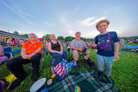 Three adults and a child in front of a blanket in a big field with more people behind and a near-sunset sky with a few cirrus clouds