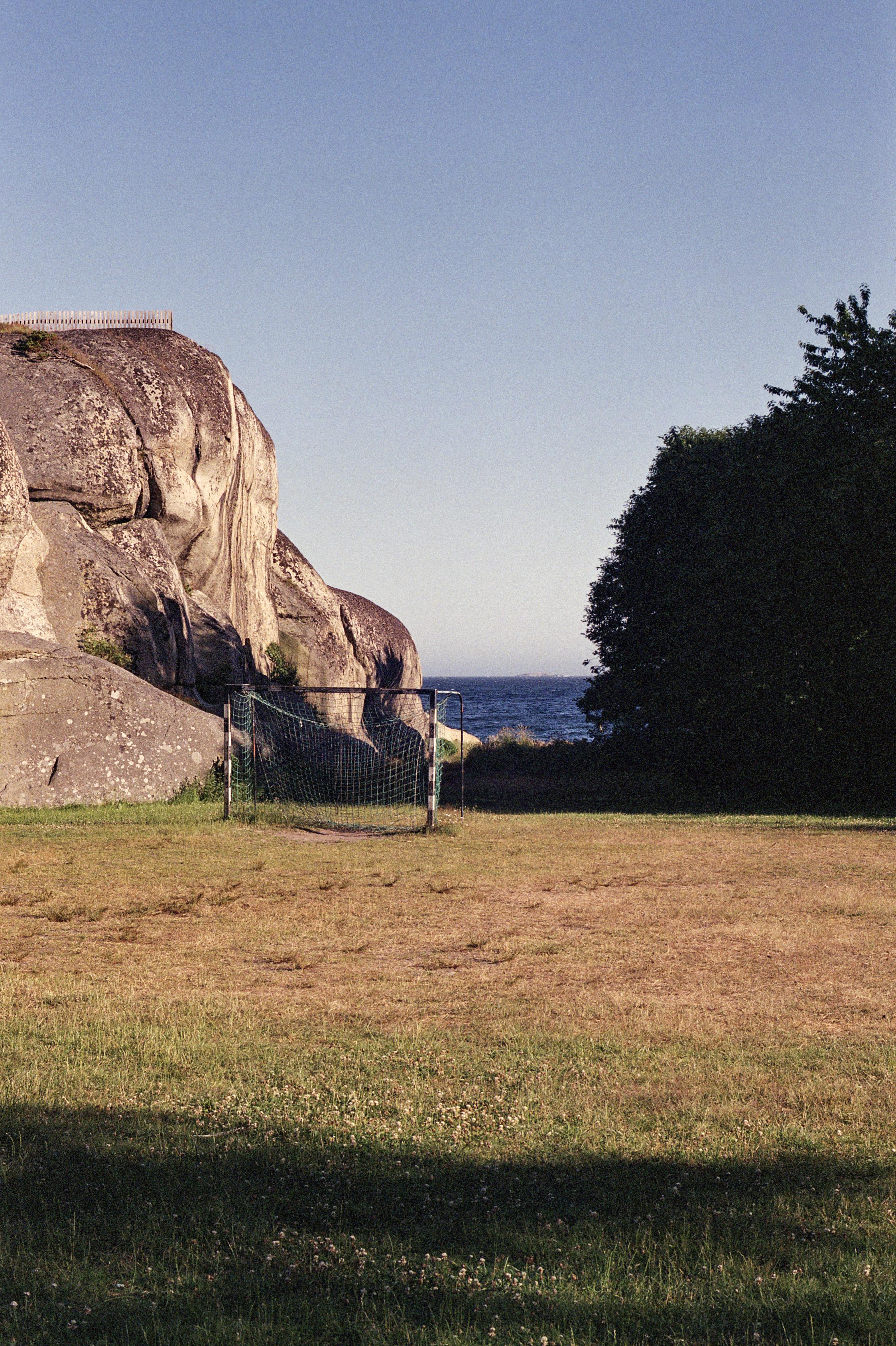 A goal on a field in front of a cliff and a forest. View of the sea in between. Sunny summer weather and blue sky.