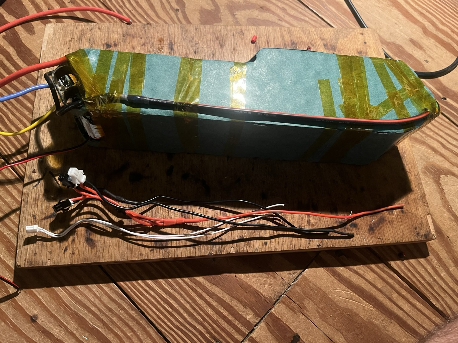 Side of battery pack with fish paper covering the terminals and negative discharge wire attached to the BMS. Beside the pack is a bunch of thinner wires with connectors on one end.