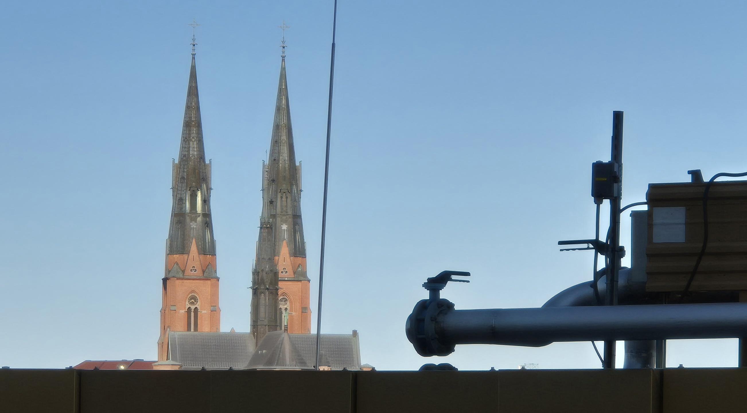 Uppsala cathedral in the morning sun, raising above service machinery atop a nondescript foreground roof.