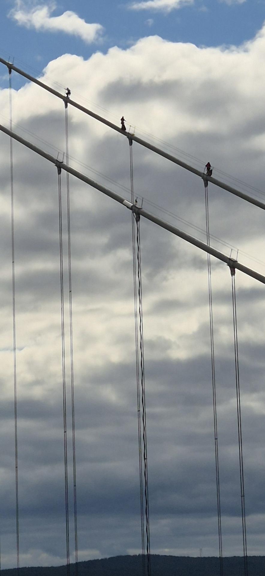 Detail of the suspender cables, three human figures barely visible at the top.