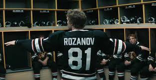 Ilya Rozanov spreads his arms for attention in a hockey dressing room in a scene from the drama-romance TV show, “Heated Rivalry.”