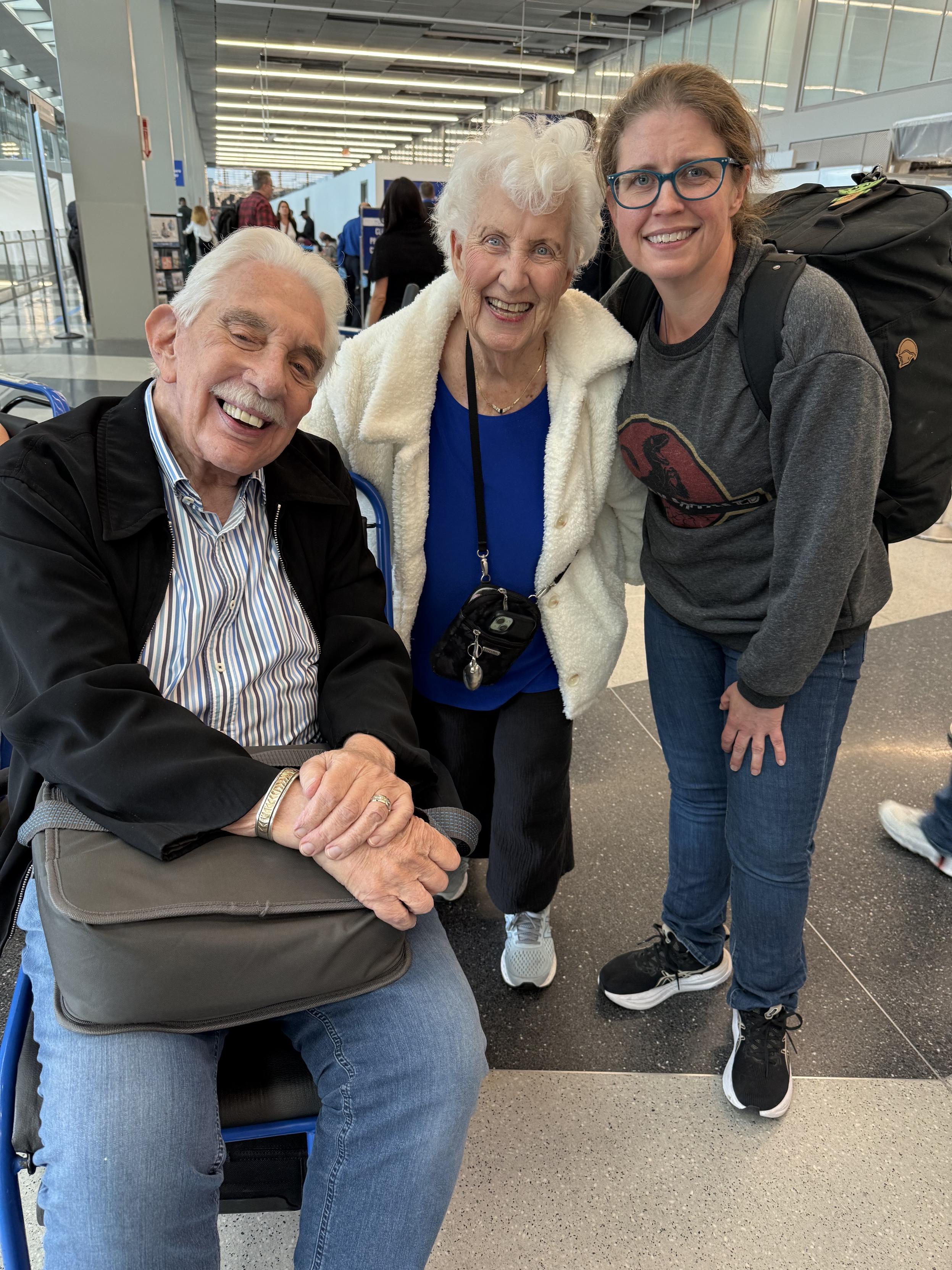 A man and two women standing next to each other with an airport scene in the background