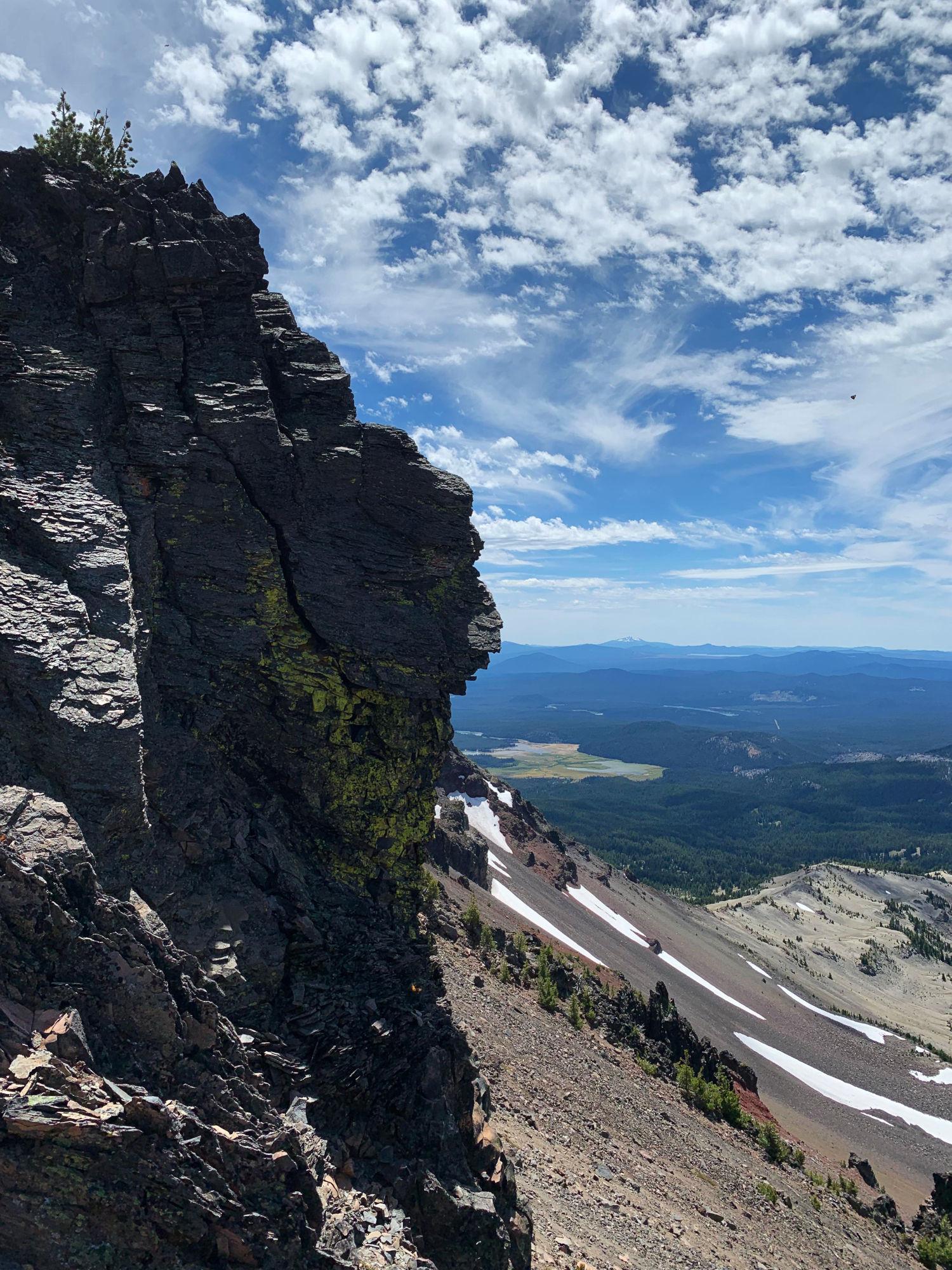 Silhouette of rock outcrop against partly cloudy sky and Broken Top skree slope