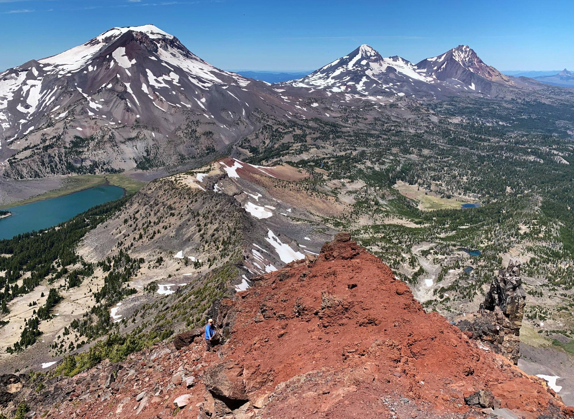 The Three Sisters from high up the ridge going up Broken Top. The Ridge has a layer of crumbly red rocks. Green Lake is down between Broken Top and South Sister.