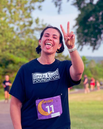 Woman with bib number 11 makes V sign and sticks out tounge with more runners on curved path behind her