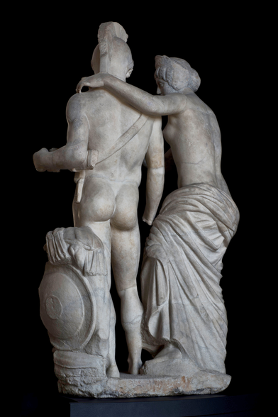 Mars and Venus marble sculpture group, dated ca. 170 CE from the Terme di Diocleziano. They are seen from the reverse in this photo against an all black background. Venus has her arm draped over Mars' shoulder who wears nothing but a sword belt.