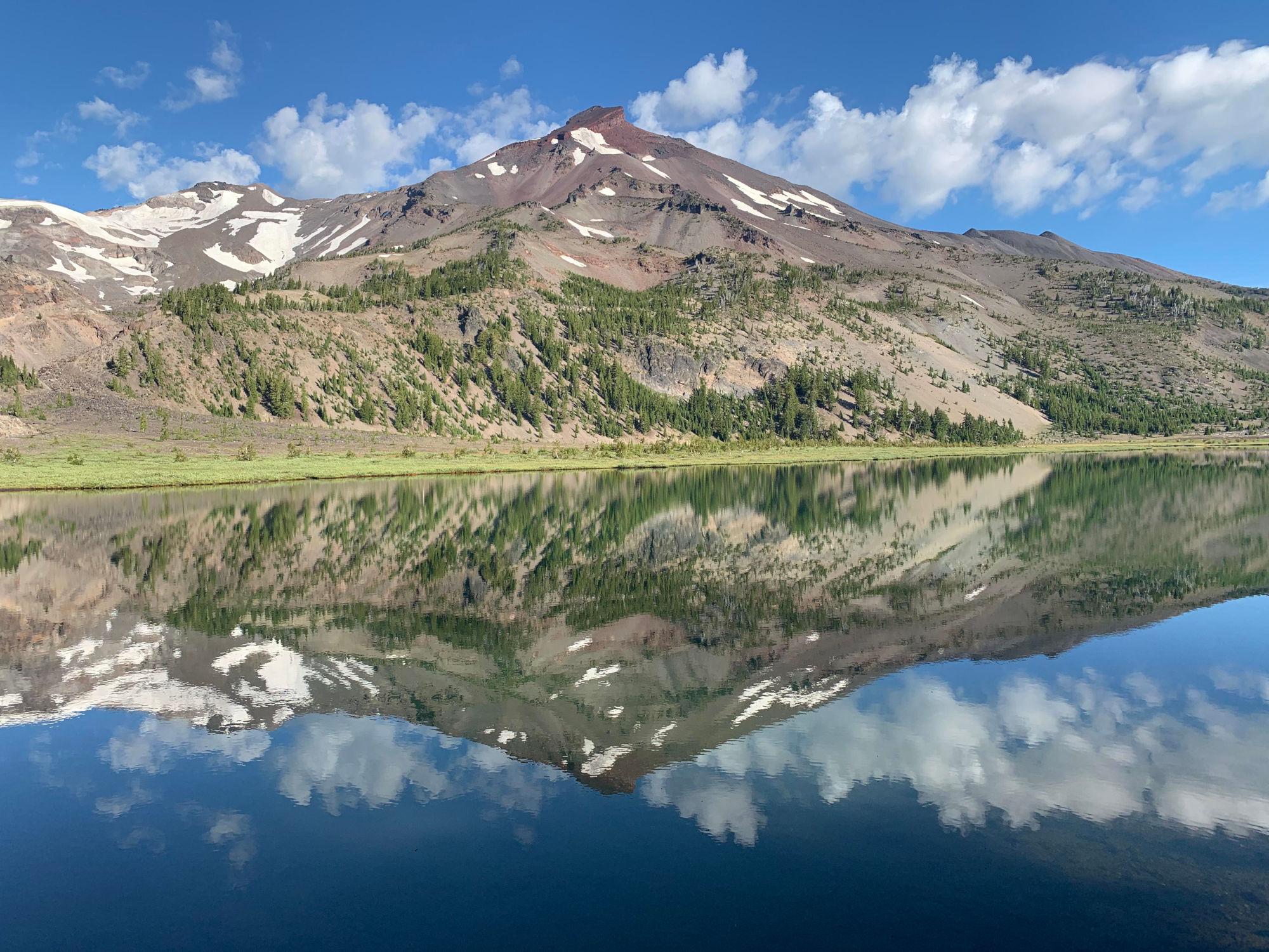 South Sister reflected in a very still Green Lake under mostly blue sky in the morning.