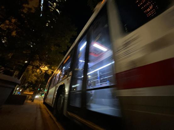 cta bus driving past with the interior clearly lit by overhead lighting. the street is mostly lit by sodium vapor lighting making the coloring wonky