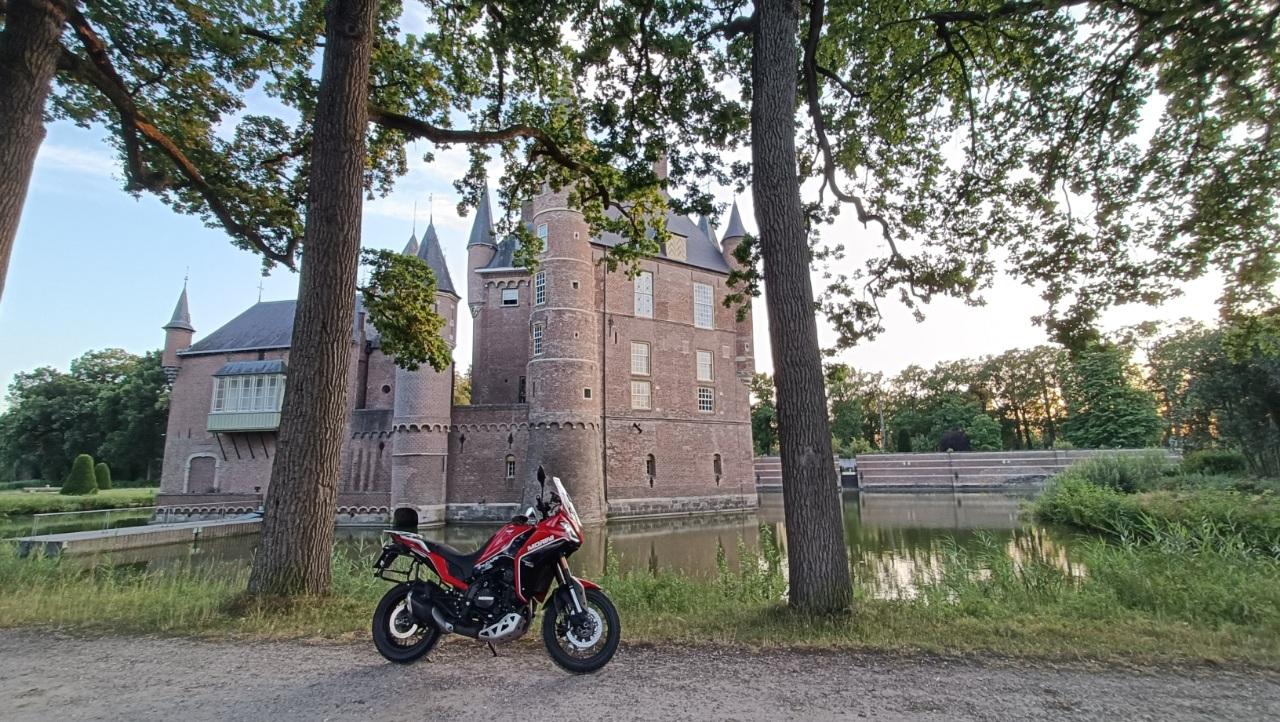 Rid bike between trees along a moat with a big medieval castle behind
