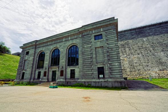 Big granite block building with three round-topped windows in front of dam surrounded by grass