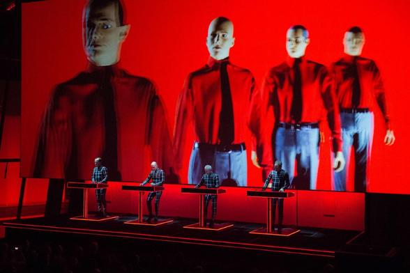Four lecterns side by side, against a red background. Men in suits (this is Kraftwerk)