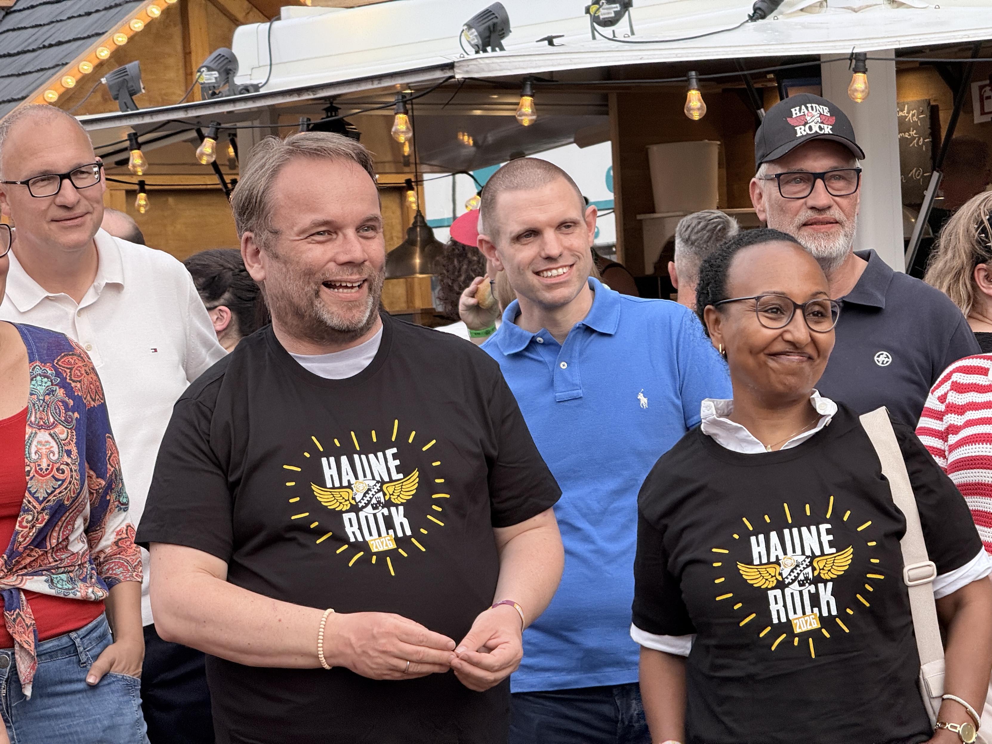 Eine Gruppe von Menschen versammelt sich im Freien, lächelte und trug T-Shirts mit dem Logo "Haune Rock" prominent. Es sind Minister Timon Gremmels und Awet Tesfaiesus.
