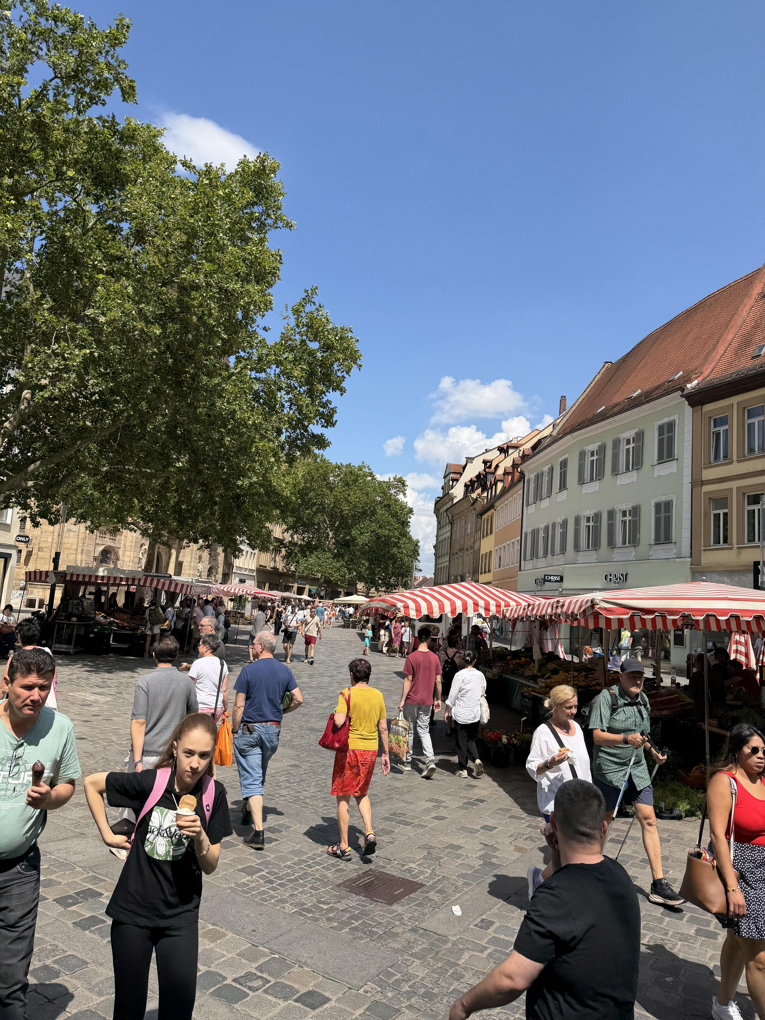 Menschen gehen auf einem belebten Marktplatz mit Ständen im Freien und roten und weißen Markisen.