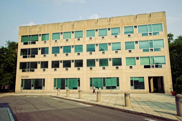 Light colored concrete building with windows that have a dark cast on the lower left towards a light blue cast on the upper right