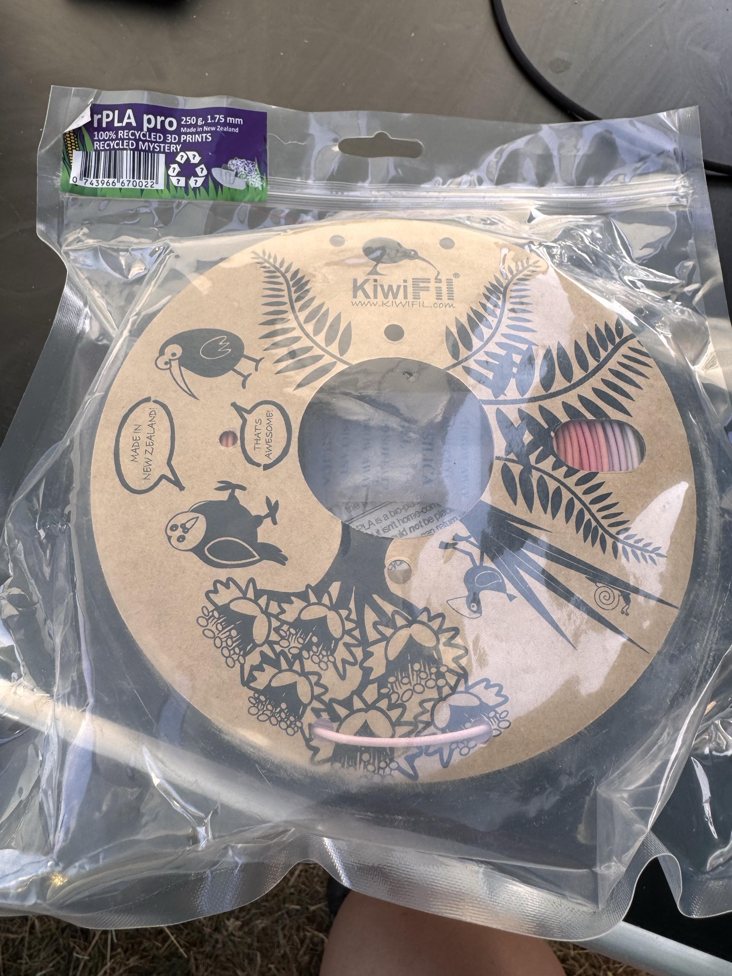 A spool of rPLA pro 3D printing filament in a clear plastic packaging. The spool has a decorative design featuring birds and flowers. The label indicates it is made from 100% recycled materials in New Zealand, with specifications of 250g