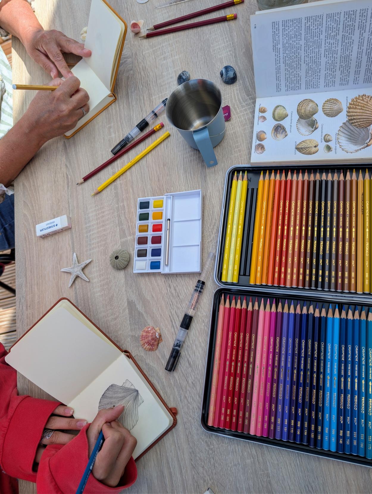 Mensen werken in een schetsboek, potloden, aquarel en jutvondsten op de tafel