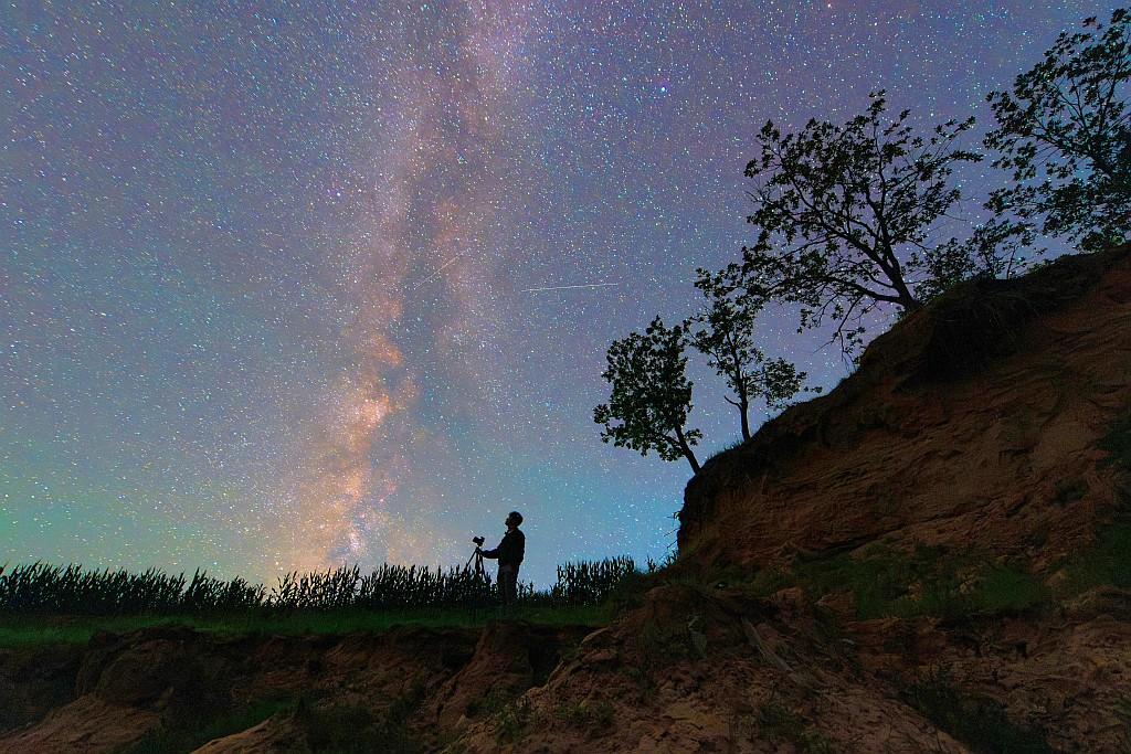 A silhouette of a photographer with a tripod & camera and the Milky Way.