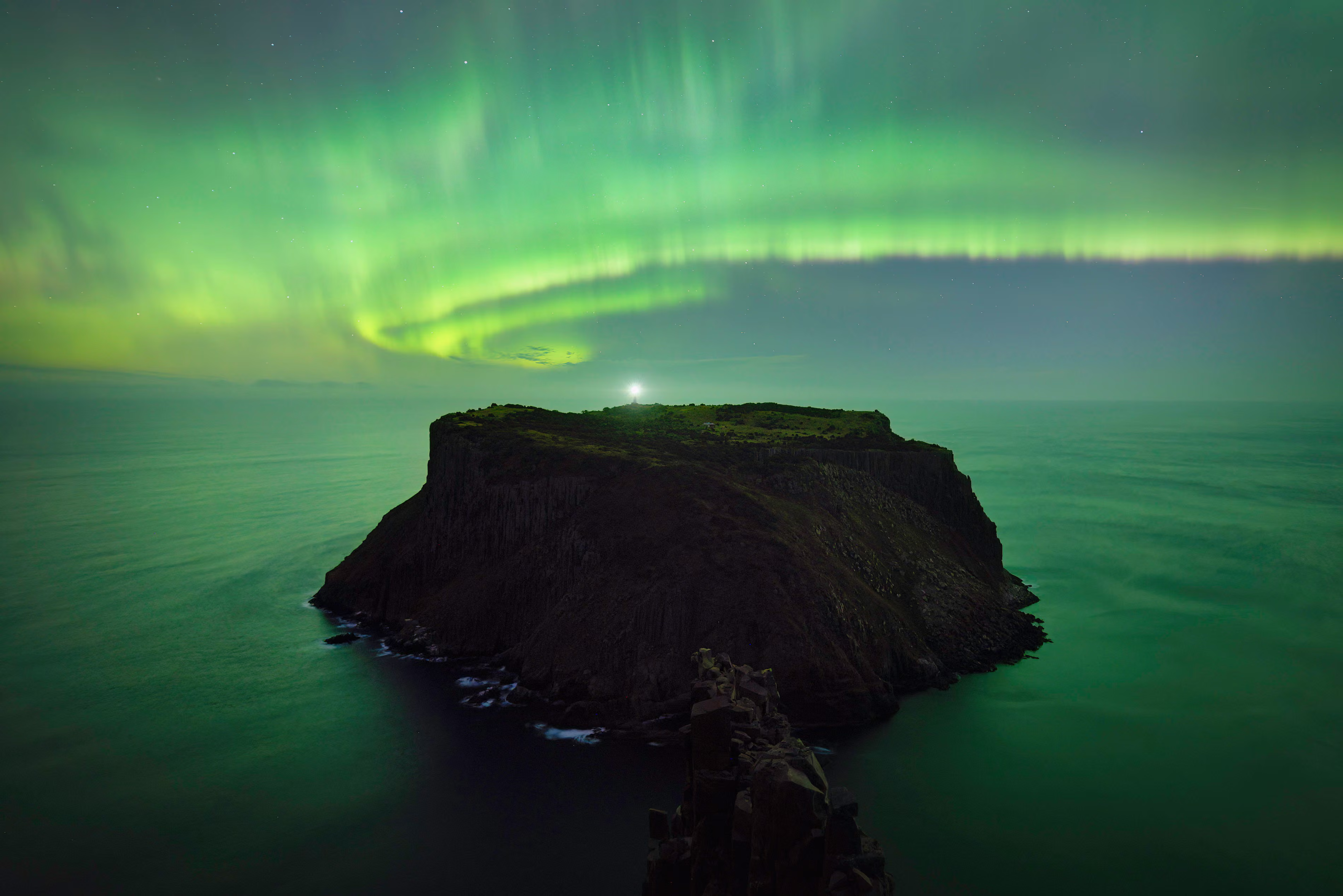 Atop Australia’s tallest sea cliffs, the aurora australis arcs across the sky, its curtain sweeping down as if to touch the Tasman Island.