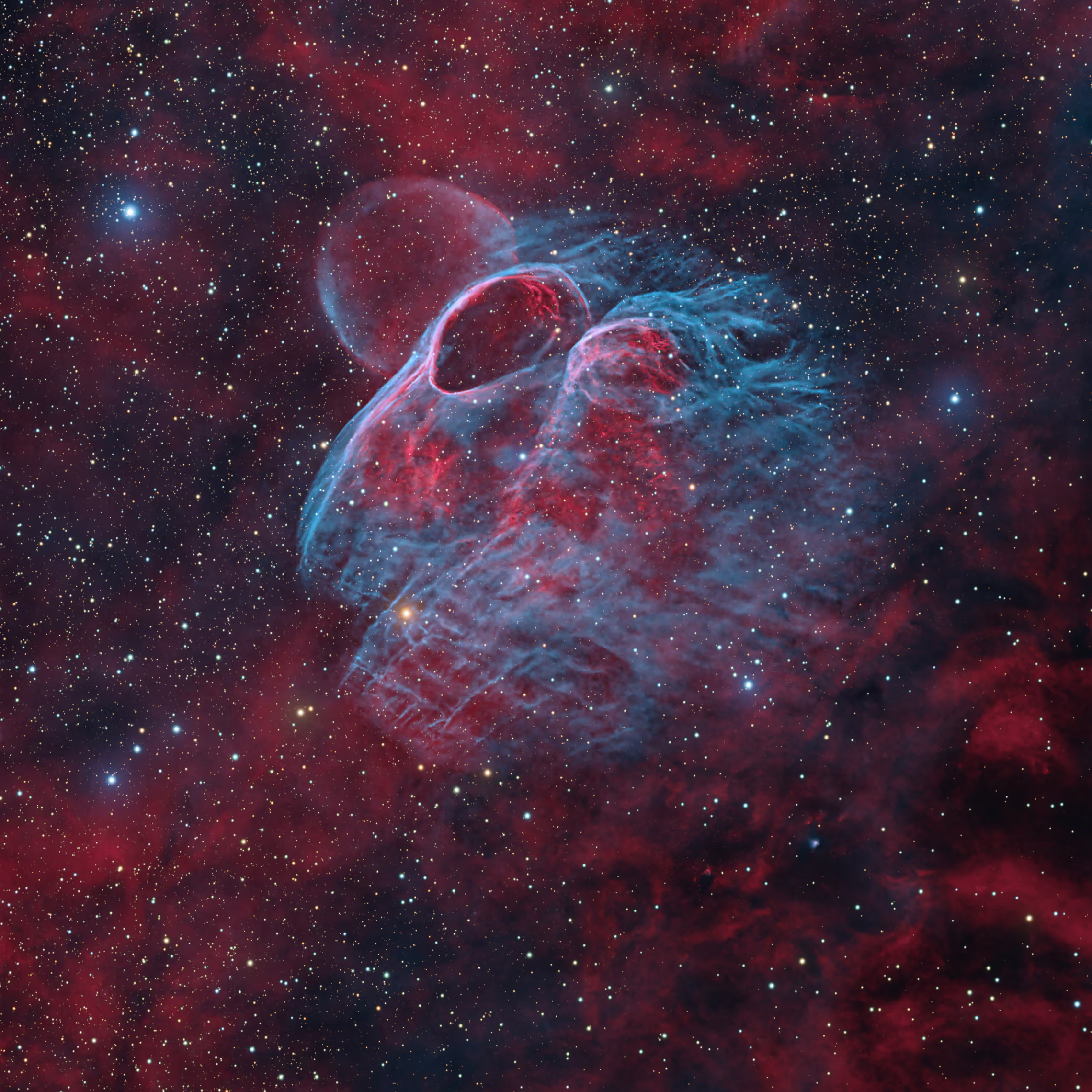 A deep-space photograph showing delicate shockwave filaments near the newly discovered OED-1 nebula structure in Vela. At the center, vibrant cyan and turquoise oxygen gas forms intricate ring-like arcs and fine, wispy tendrils. Glowing red hydrogen gas fills the surrounding space, complemented by a faint reddish spherical shell hovering just above the main blue arc, all set against a dense field of pinpoint stars.