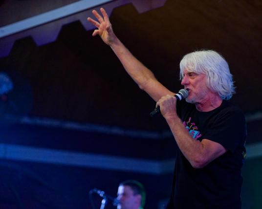 Man white moderate length white hair has arms up in the air
