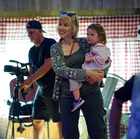 In the center field a woman holds a small child with a video camera operator behind