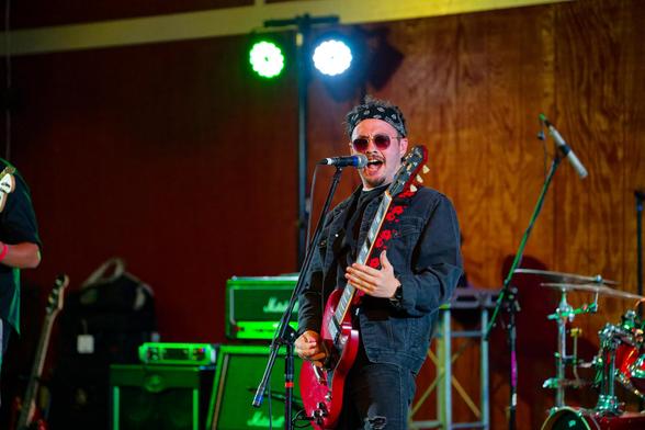 Wide shot of man with bandanna playing red guitar and singing.