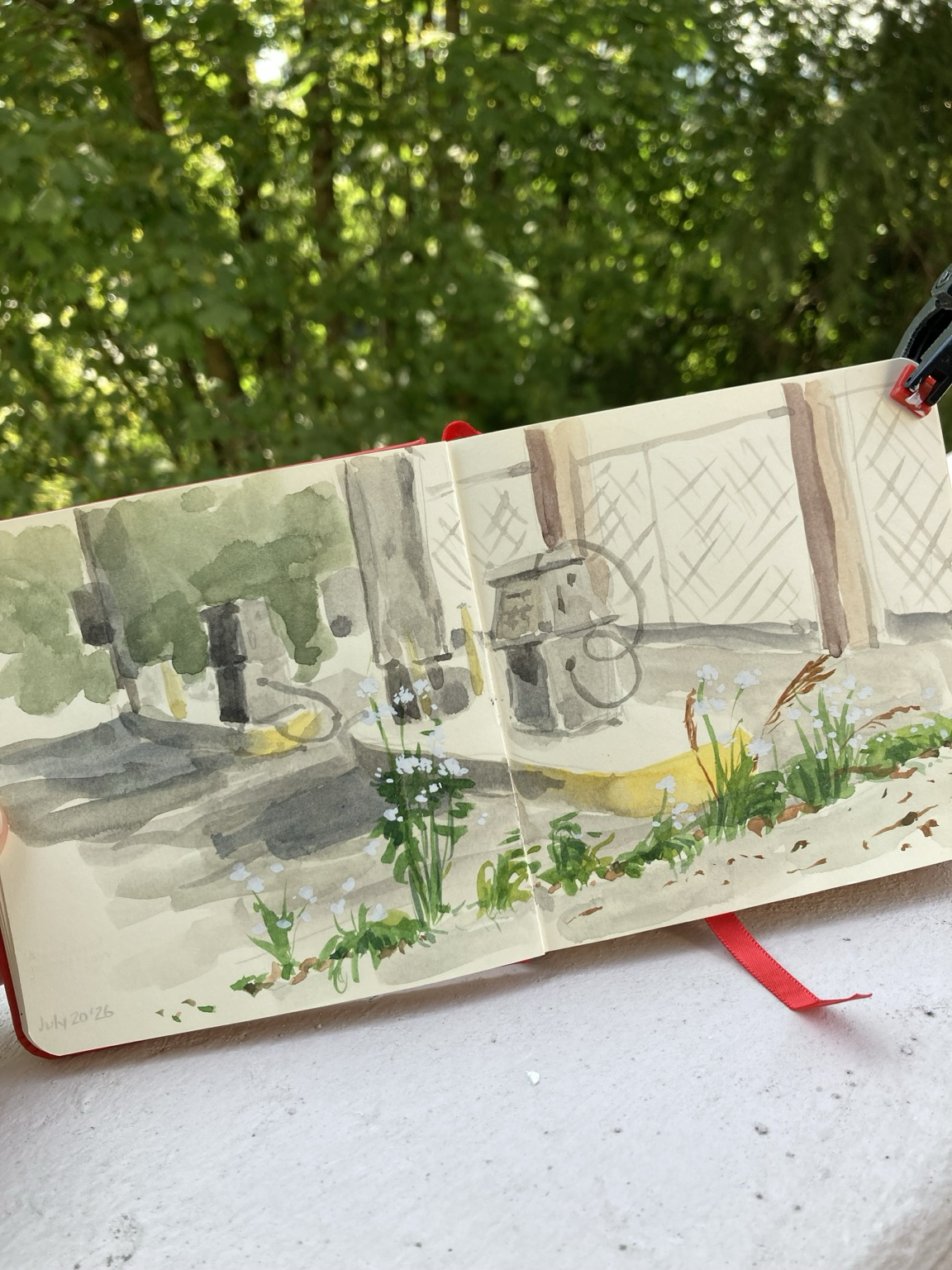 Sketchbook spread with a watercolour sketch of old gas station pumps, a fence in the background, and a row of weeds and flowers in front