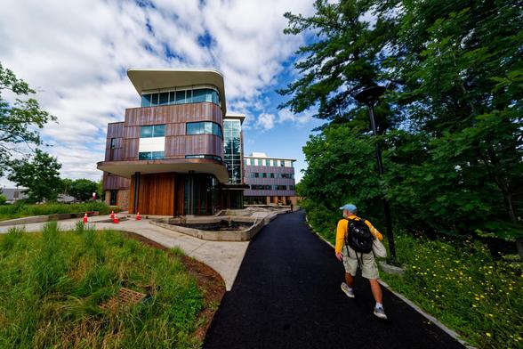 Man walks past modern seemingly copper-clad building with a stylish facade on a path that curves to the right