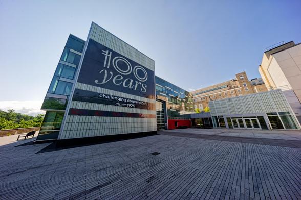 Buildings on the far side of a plaza seem hunched together in the middle including one that reads "100 years" on its side