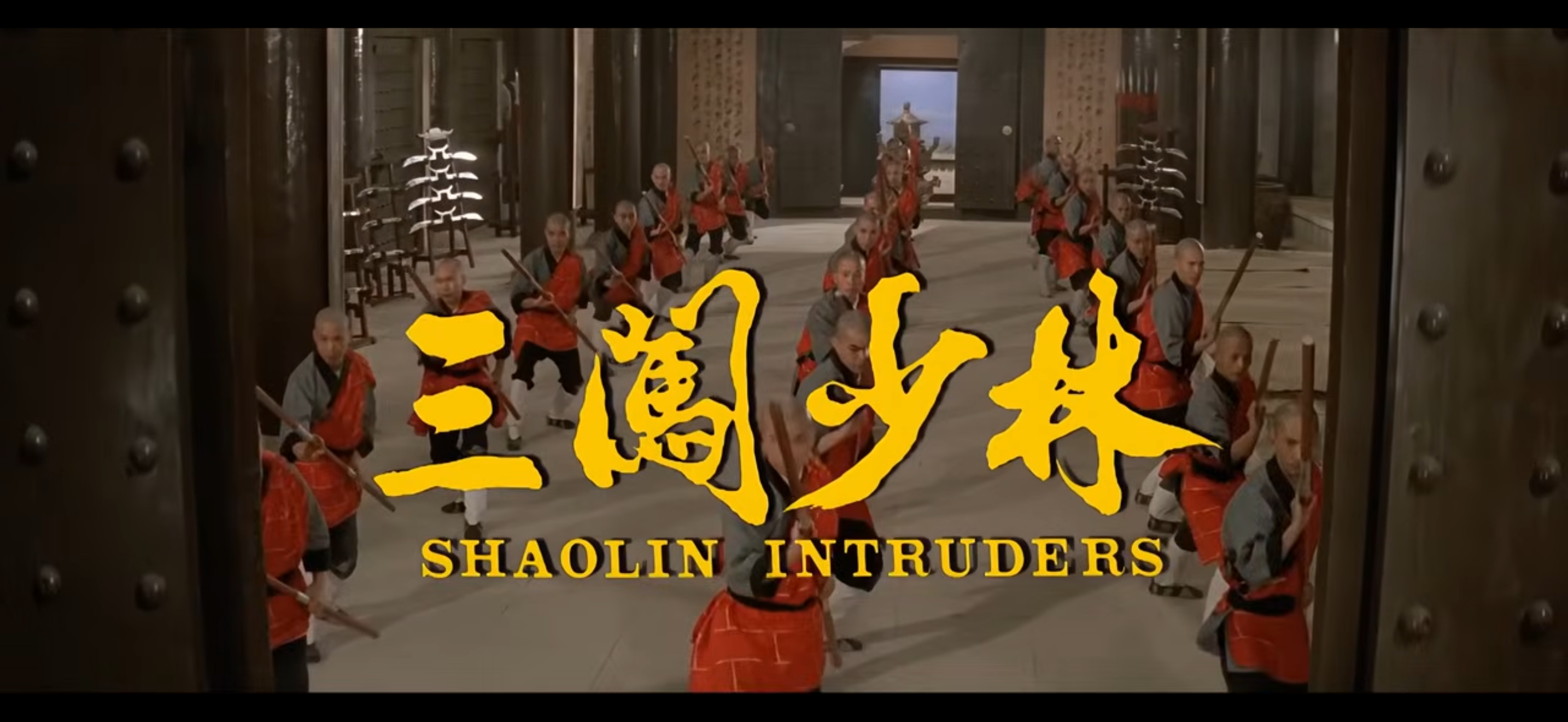 The opening scene from the 1983 Shaw Brothers film "Shaolin Intruders" featuring several dozen martial artists dressed in red and gray Shaolin uniforms, practicing with wooden staffs in a traditional setting. The title "Shaolin Intruders" is prominently displayed in bold yellow letters in both Chinese and English.