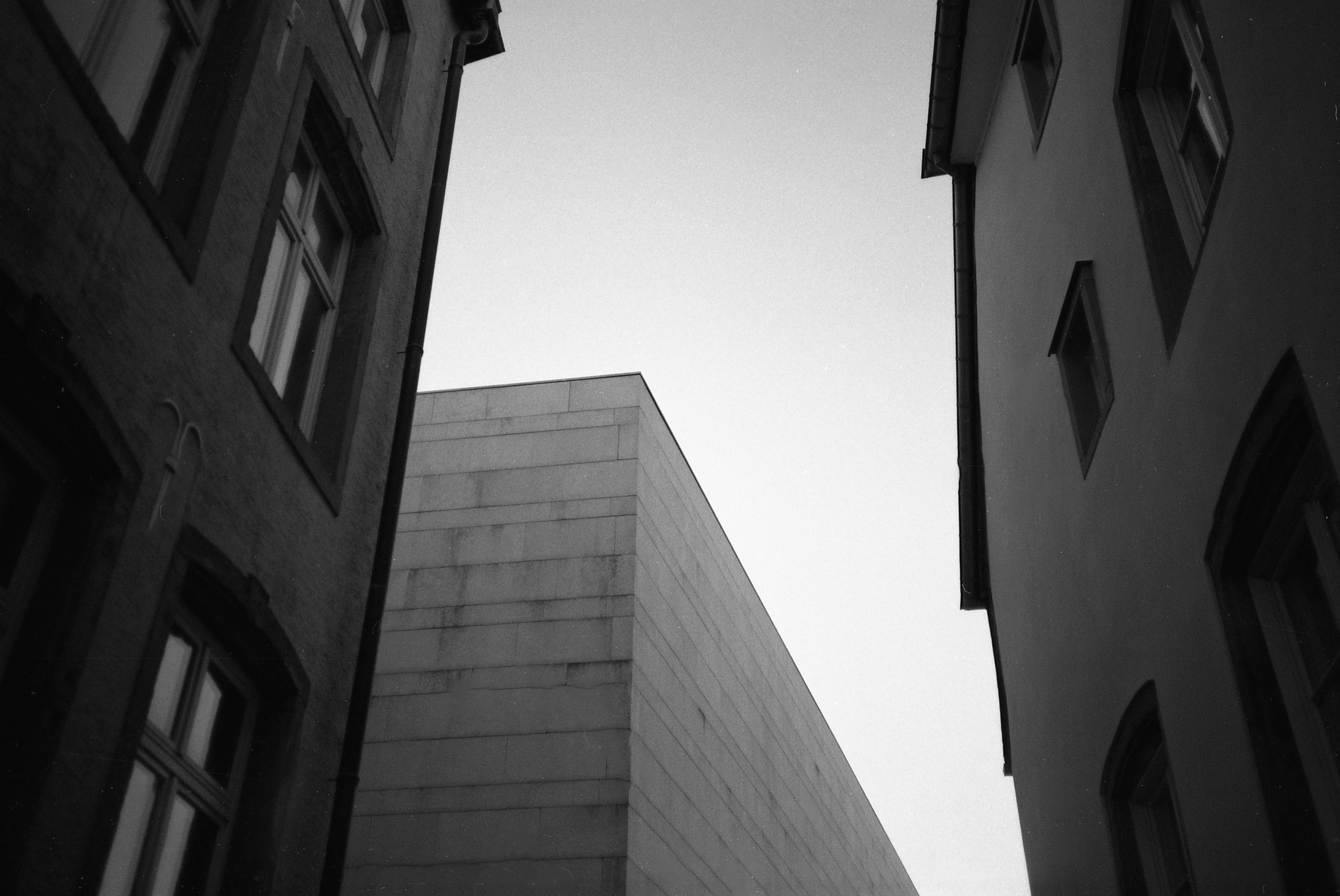 Blick nach oben zum Himmel durch eine Häuseeschlucht, rechts und links ältere Gebäude, in der Mitte ein moderner Betonbau