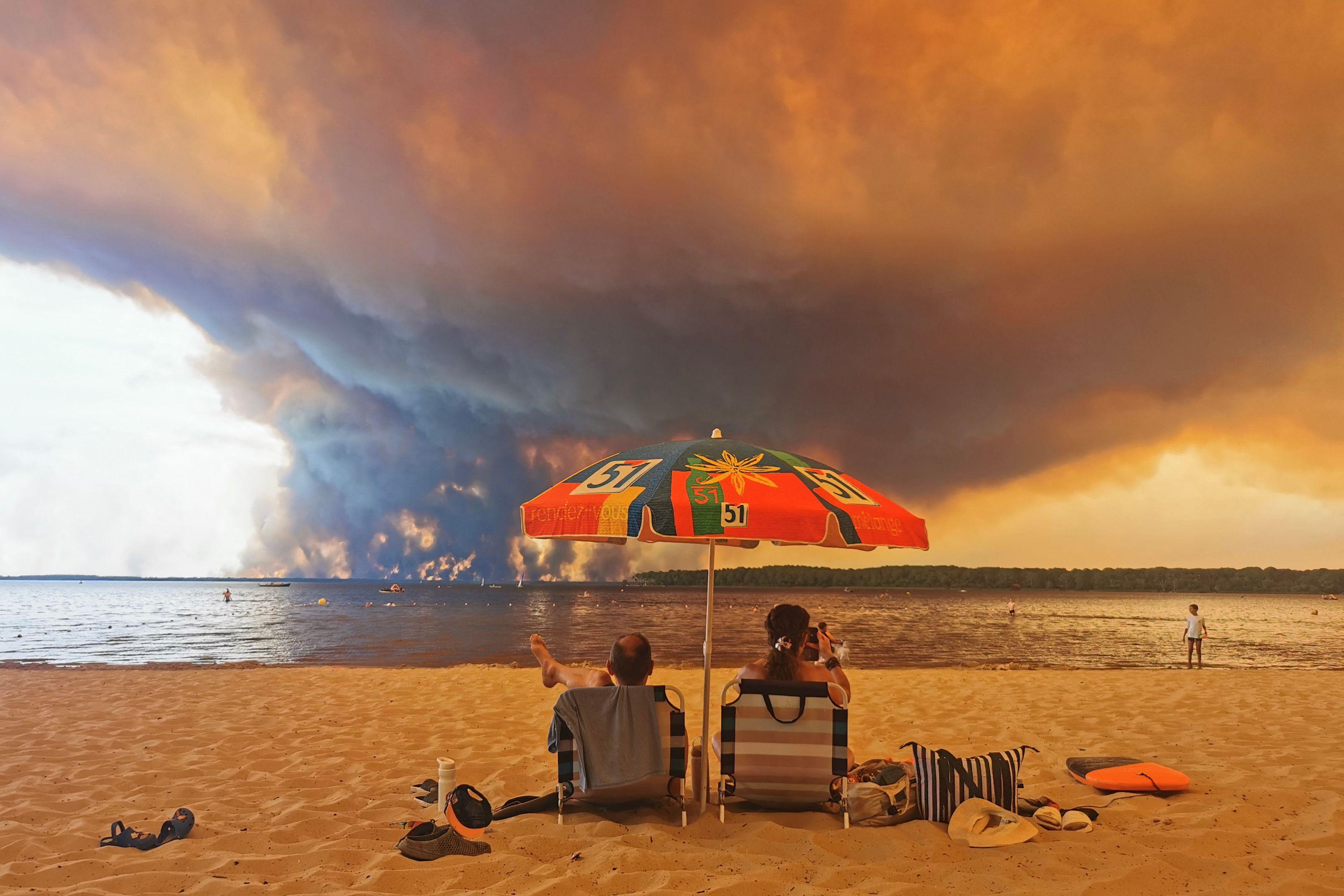 Des vacanciers sous un parasol sur la plage de Lacanau contemplent le gigantesque incendie qui ravage la région.