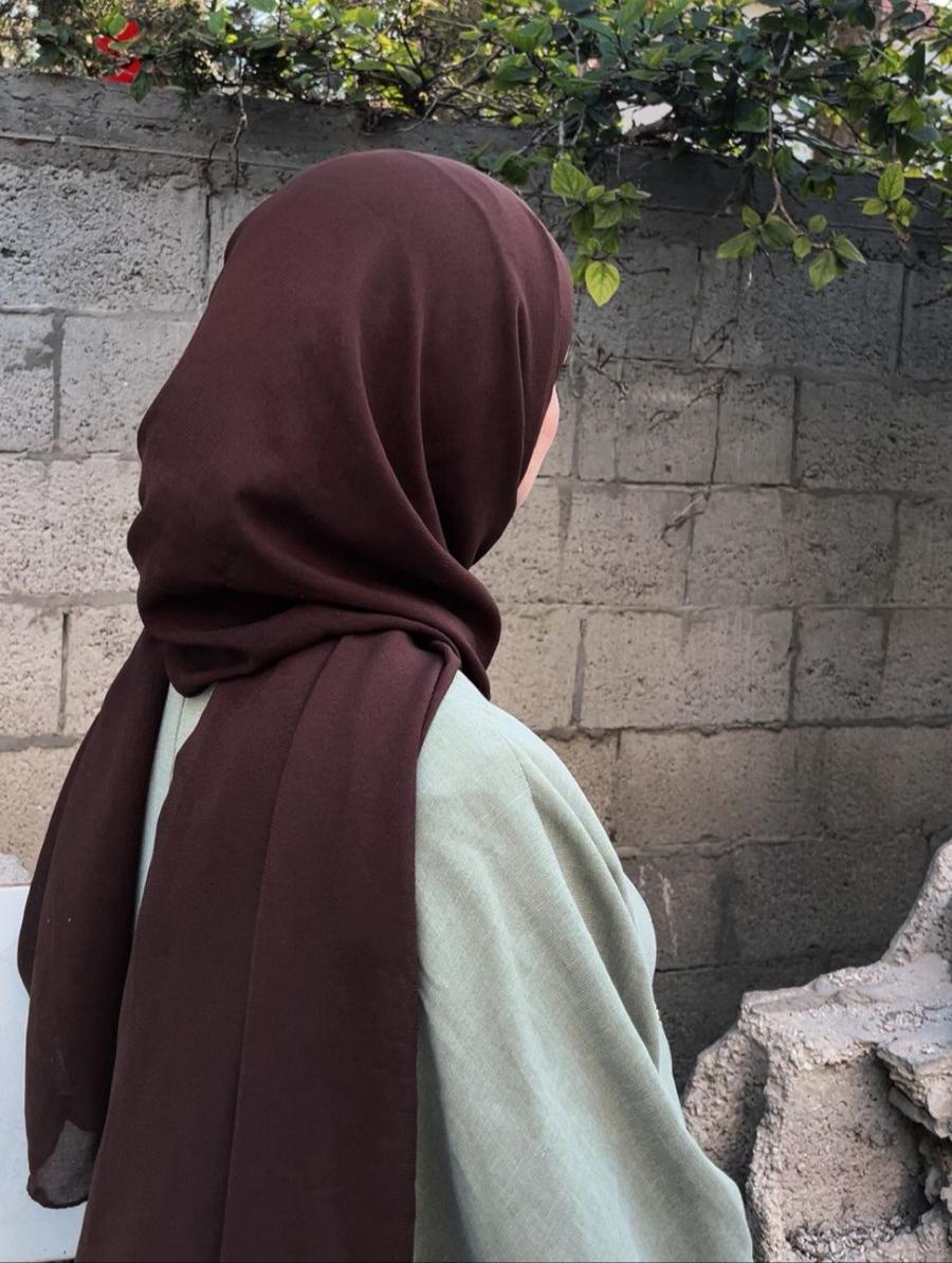 A female university student stands in front of a destroyed wall in Gaza.