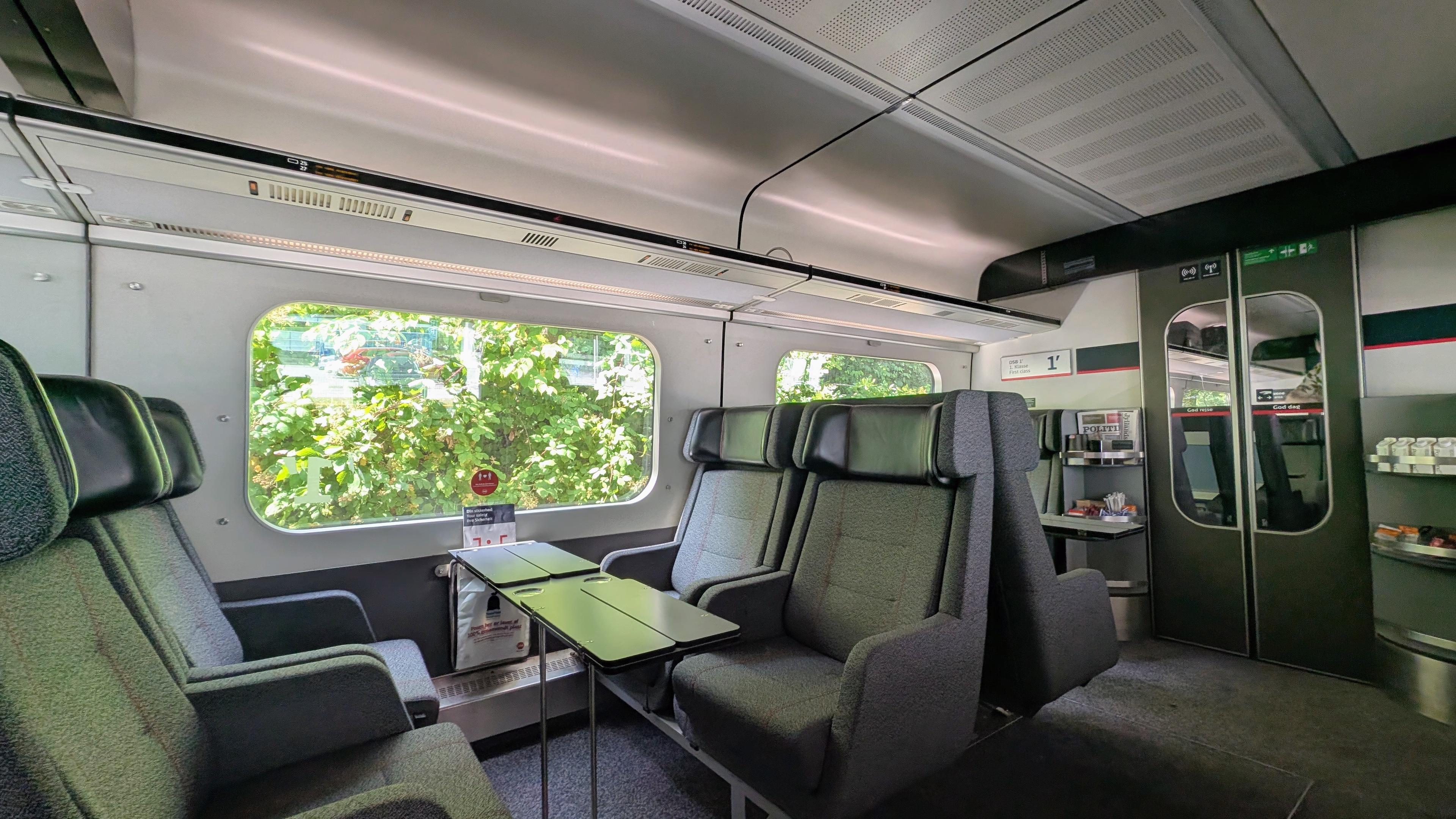 Wide-angle sight of a DSB first class Intercity interior, dark-grey seats 2+2 seating facing each other, a small foldable table in the middle