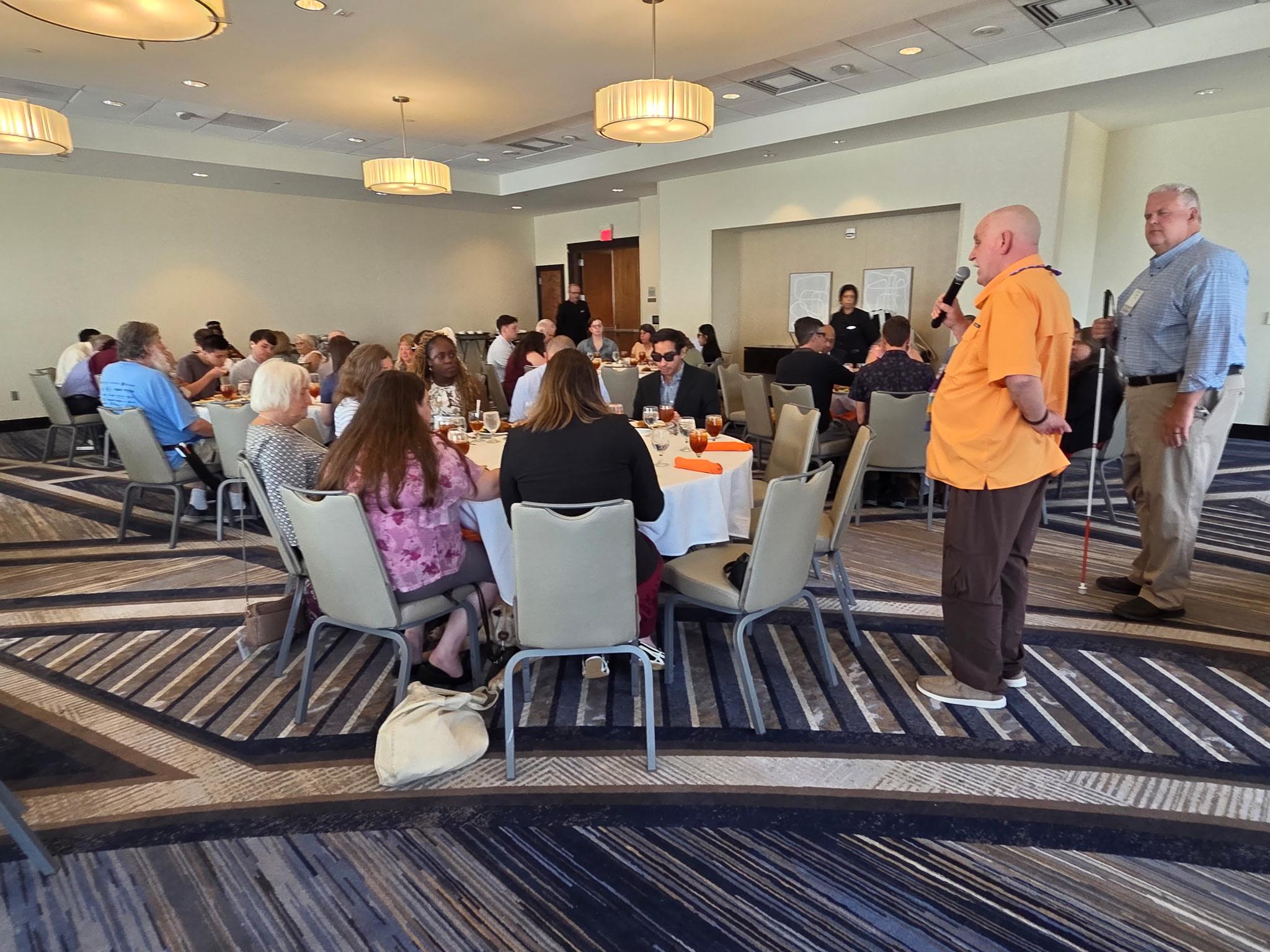 David Trott (left) and Scott Thornhill (right) speak to scholarship recipients and mentors, who are seated at large round dining tables.