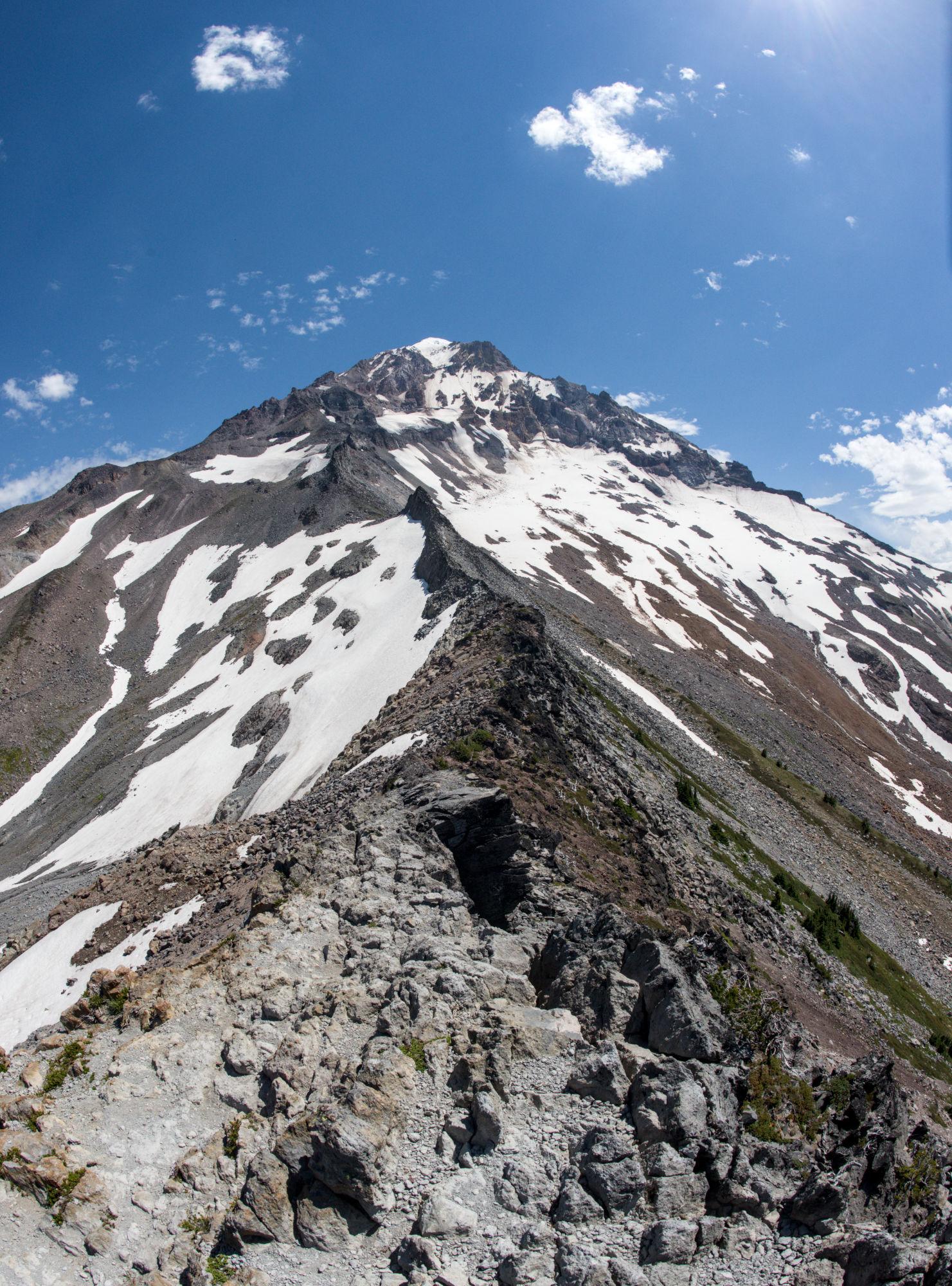 Looking up Cathedral Ridge at Mt. Hood, a rocky, spiny ridge that snakes up the slope. Patchy glaciers are on the left and right of the ridge.