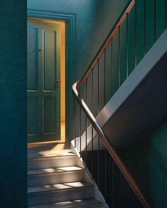 An interior staircase with deep teal walls, a curved wooden banister, and a door ajar at the top letting in warm golden light. Soft shadows.