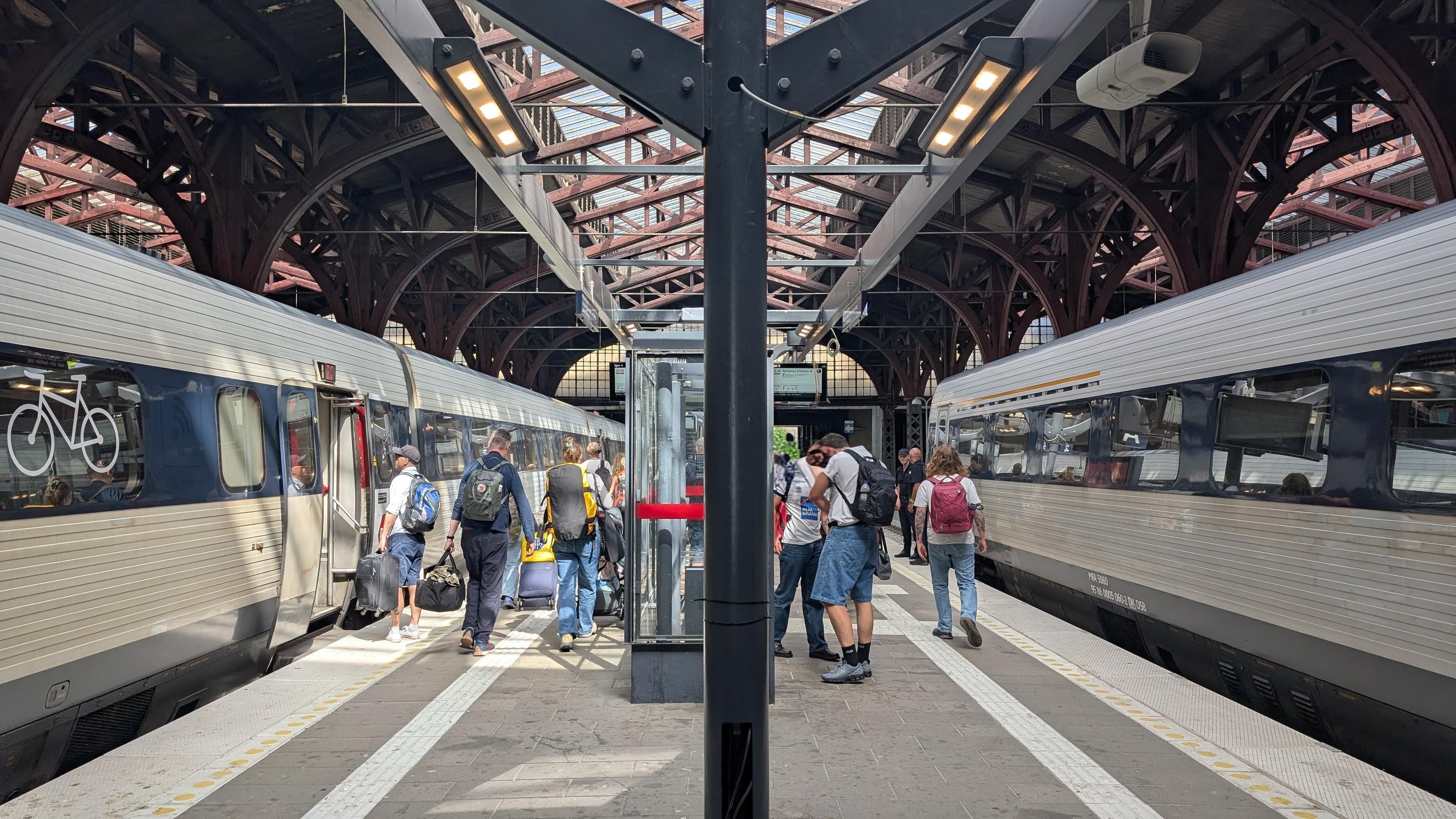 Two DSB IC3 DMU trainsets at a platform in a train shed, passenger leaving the trains and walking to the  staircase