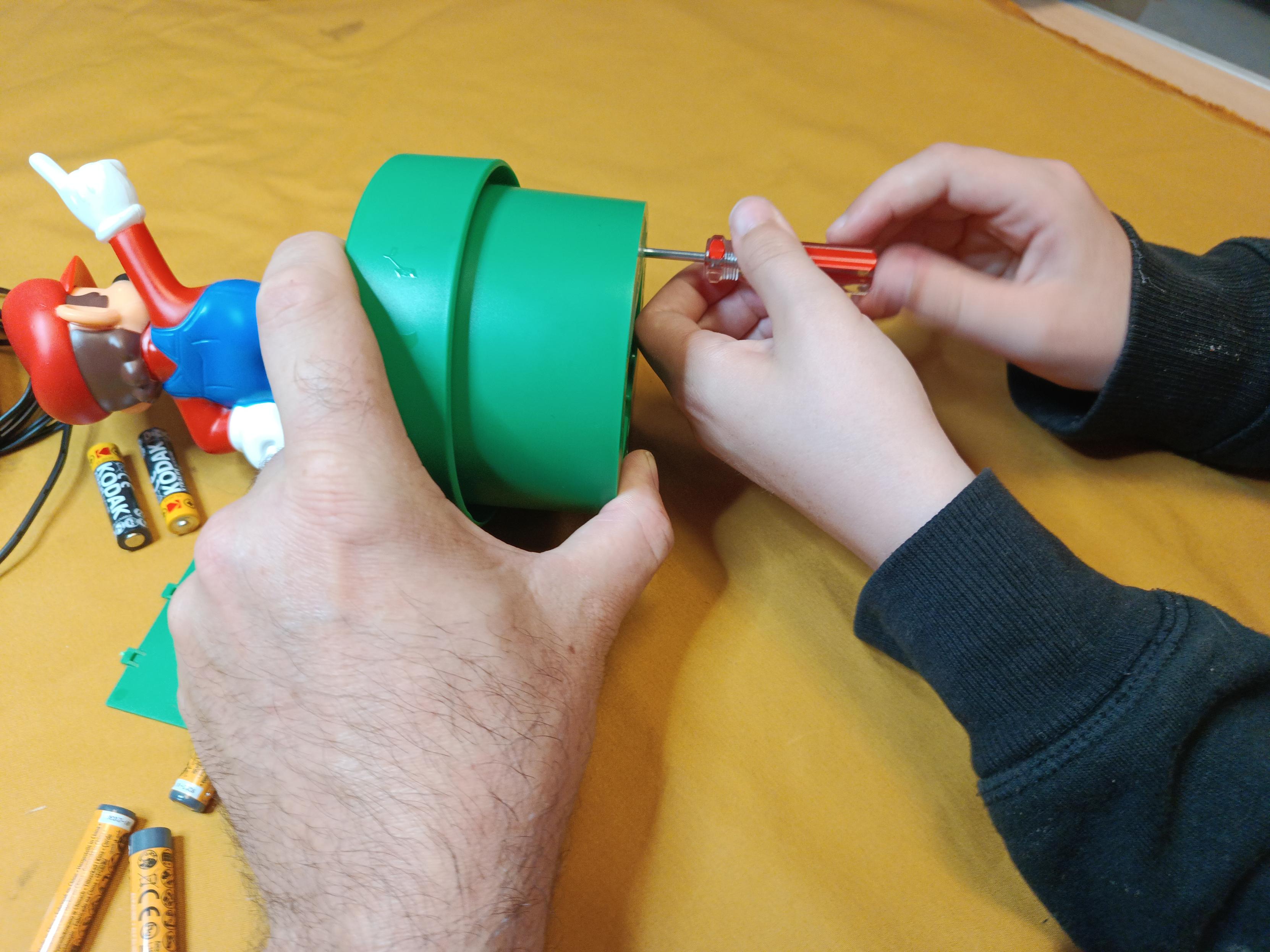 My hand holding a part whilst much smaller young person hands tighten some screws in the base of the Mario night light.